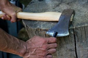 Hands sharpening an axe blade on a wooden stump, illustrating the essential maintenance work that enables sustained productivity